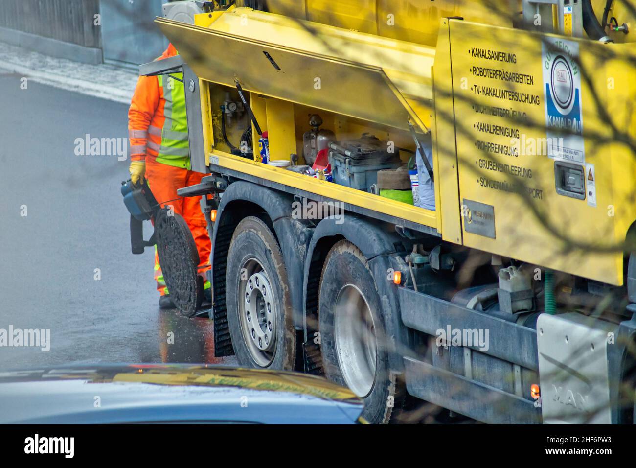 Wartung an einem Schachtloch mit einem unkenntlichen Mann, der am 16th. märz 2021 hinter dem Kanalreinigungsfahrzeug auf der offenen Straße in Oberhaching, bayern, arbeitete. Stockfoto