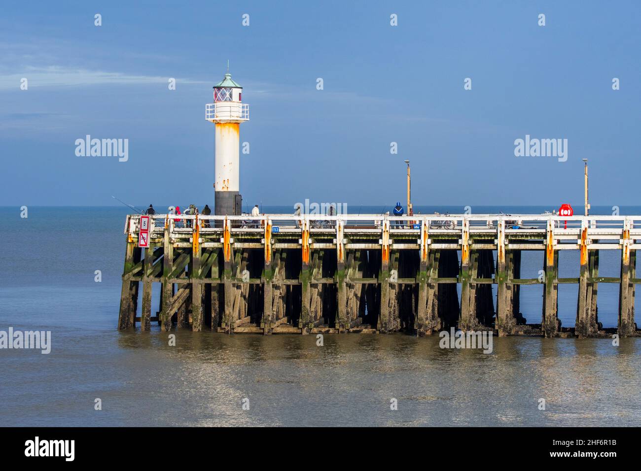 Seeangler mit großen Angelruten, die ihre Linien vom hölzernen Pier / Steg am Nieuwpoort / Nieuport Hafeneingang entlang des belgischen Nordens werfen Stockfoto