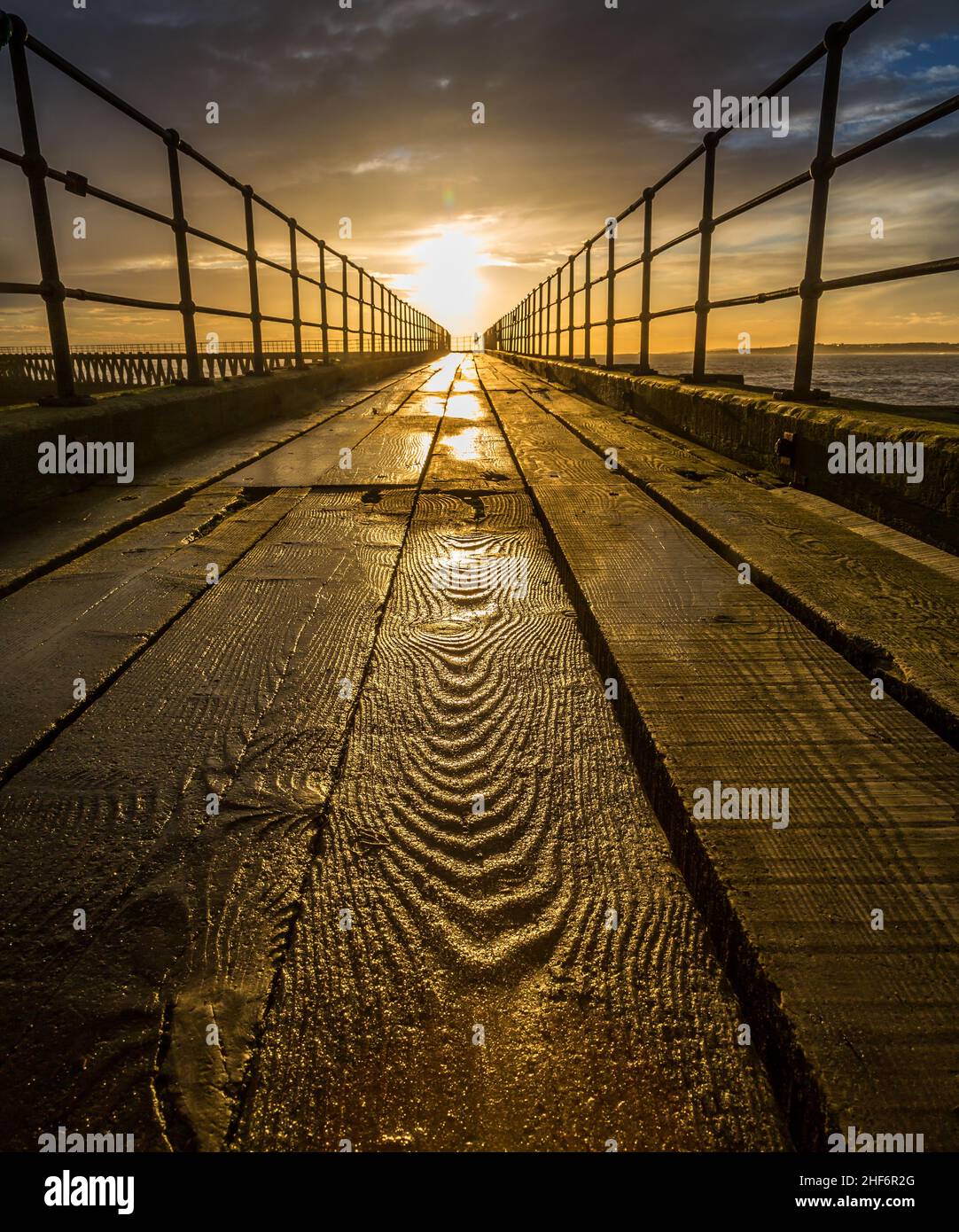 Eine Nahaufnahme einer strukturierten Holzplanke auf dem alten hölzernen Pier, der sich an einem herrlichen Morgen am Blyth Beach bis zur Nordsee erstreckt Stockfoto