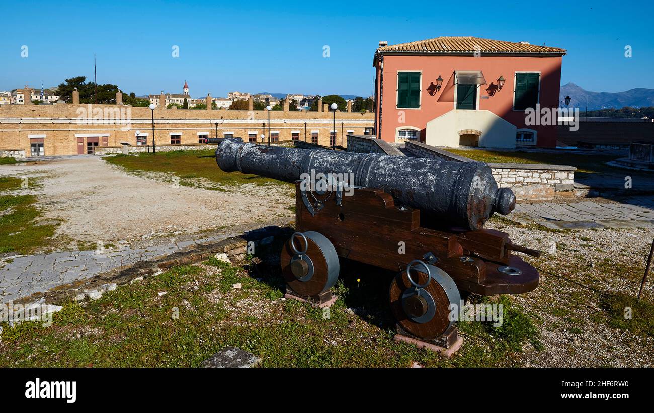 Griechenland, Griechische Inseln, Ionische Inseln, Korfu, Korfu-Stadt, Alte Festung, Kanone auf vier Rädern, rotes Gebäude oben rechts im Hintergrund, Festungsmauern, blauer Himmel Stockfoto