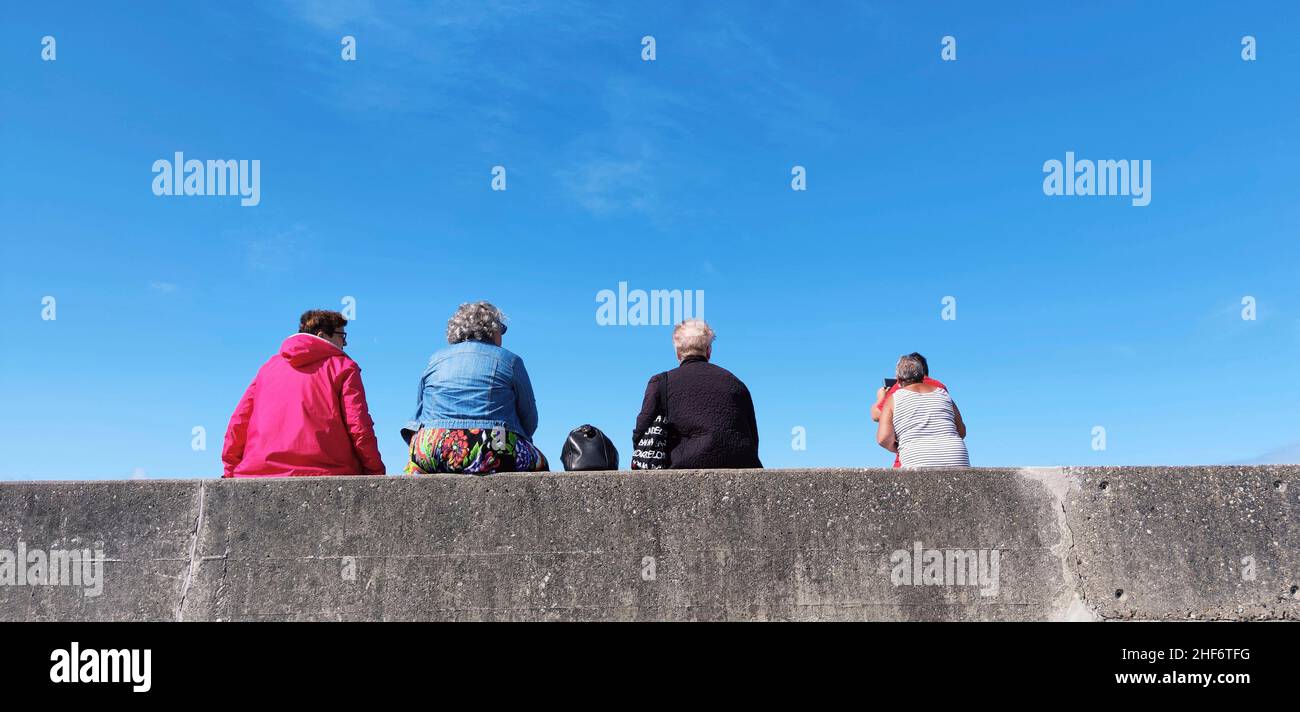 Menschen sitzen an der Kaimauer mit Blick auf das Meer, Frankreich, die Normandie, Cote d'Albatre, Quiberville Plage Stockfoto