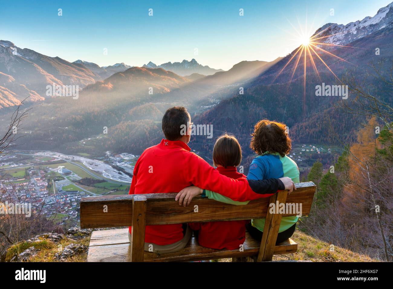 Dreiköpfige Familie (Mutter, Vater und Tochter), die im Herbst auf einer Bank sitzt und den Sonnenuntergang beobachtet, Agordo, Provinz Belluno, Venetien, Italien Stockfoto