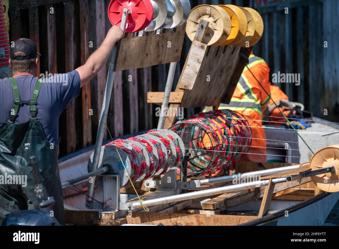 Ein Fischer steht mit seiner Hand auf der Kurbel einer Tintenfischwadenmaschine mit Rollen, Wadeneinhängern und Platinen. Die Maschine besteht aus Kunststoffrädern. Stockfoto