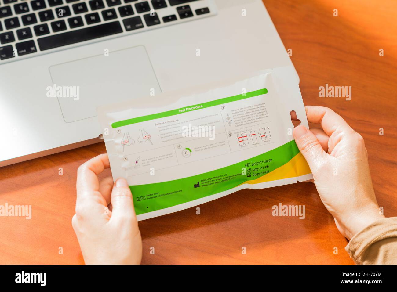 Sevilla, Spanien. 28. Dezember 2021. Detail der Hände einer Frau, die ein Covid19-Antigen-Selbsttest-Kit vor einem Laptop hält und Informationen über das Gerät betrachtet Stockfoto