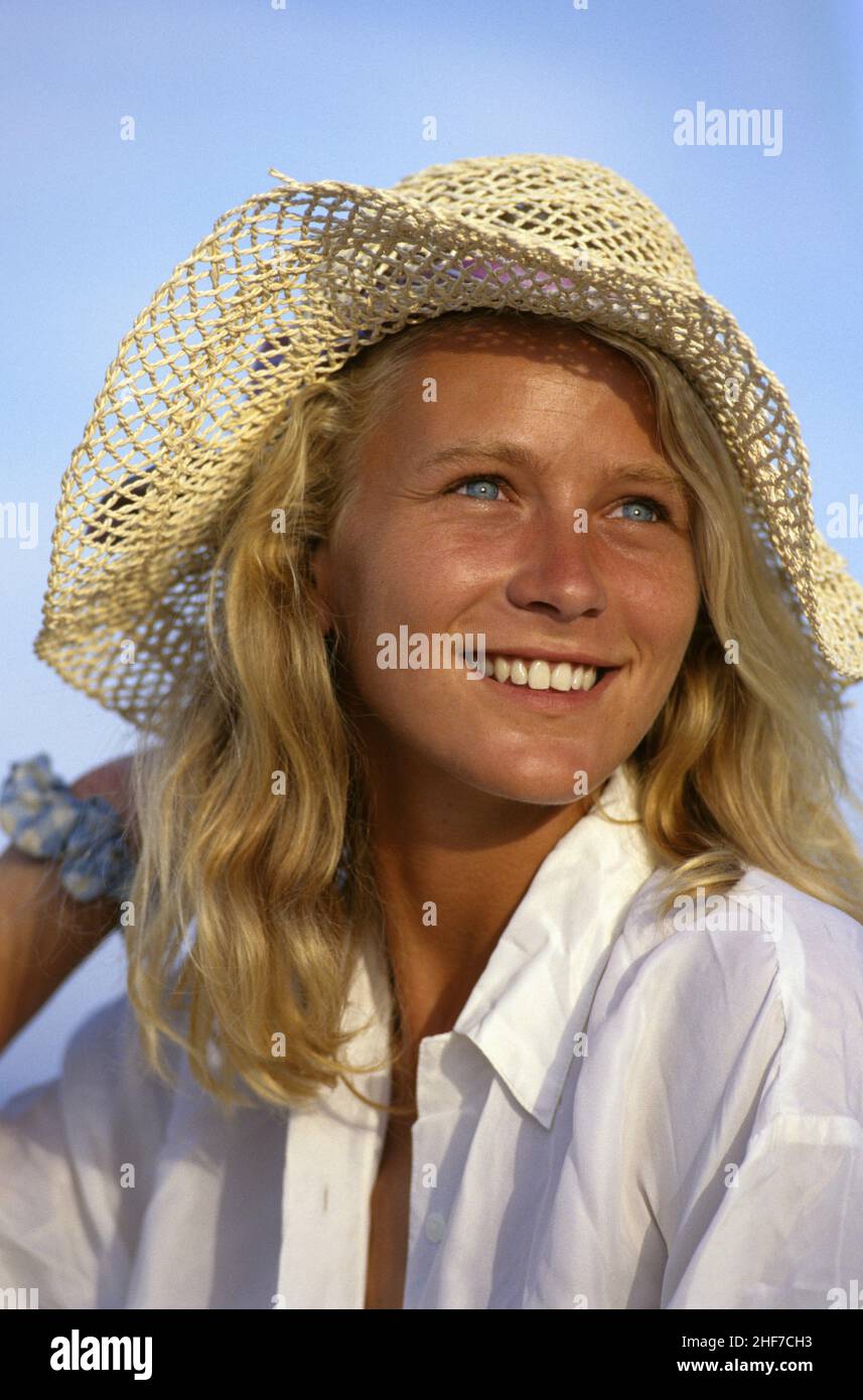 Attraktive blonde Haare junge Frau lächelndes Gesicht Porträt Sonne Licht durch Strohhut projizieren Fleck von hellblauen Augen süß aussehend Stockfoto