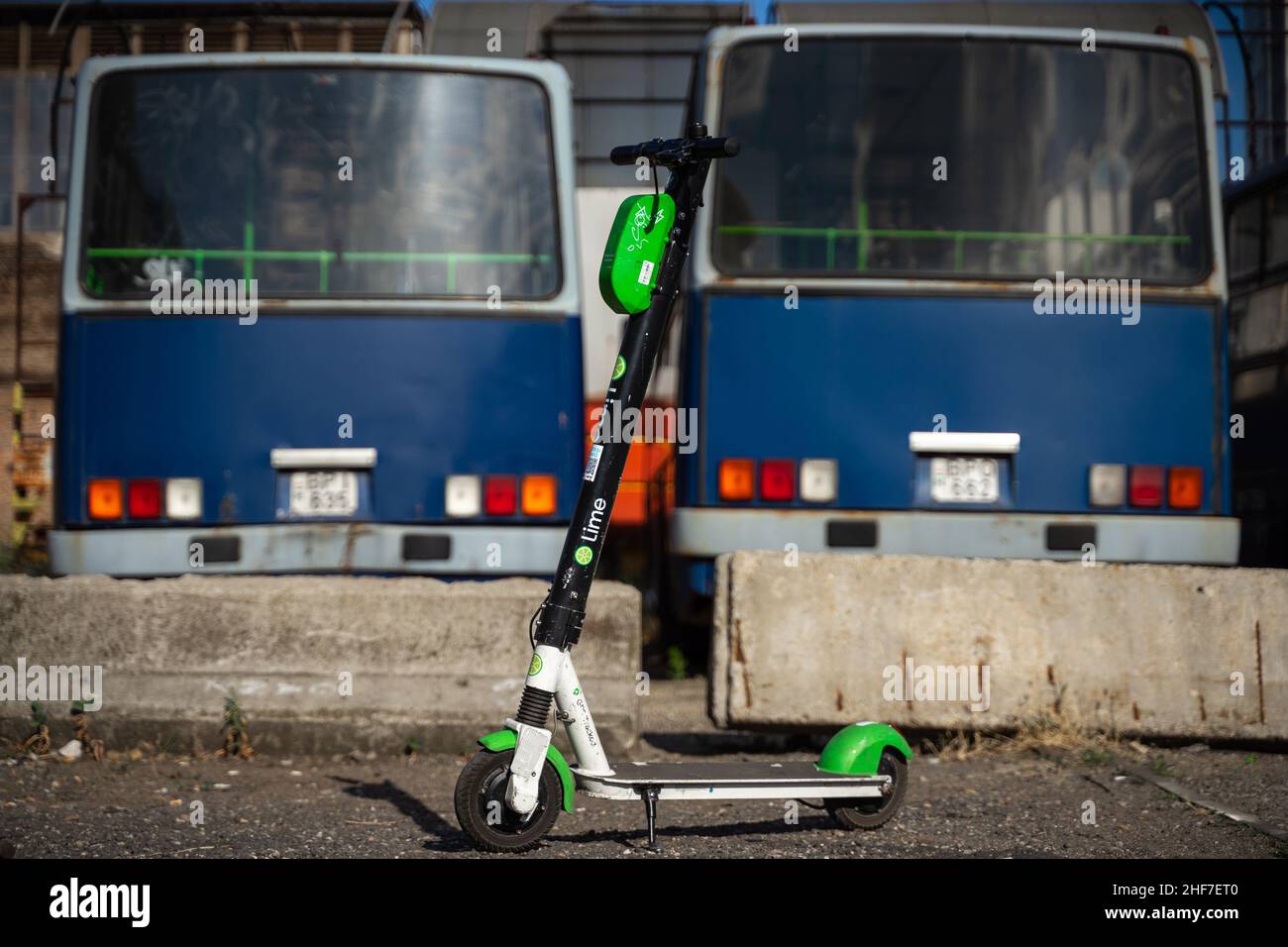 Budapest Transport damals und heute: Moderner Elektroroller mit alten, ungenutzten Bussen im Hintergrund. Stockfoto