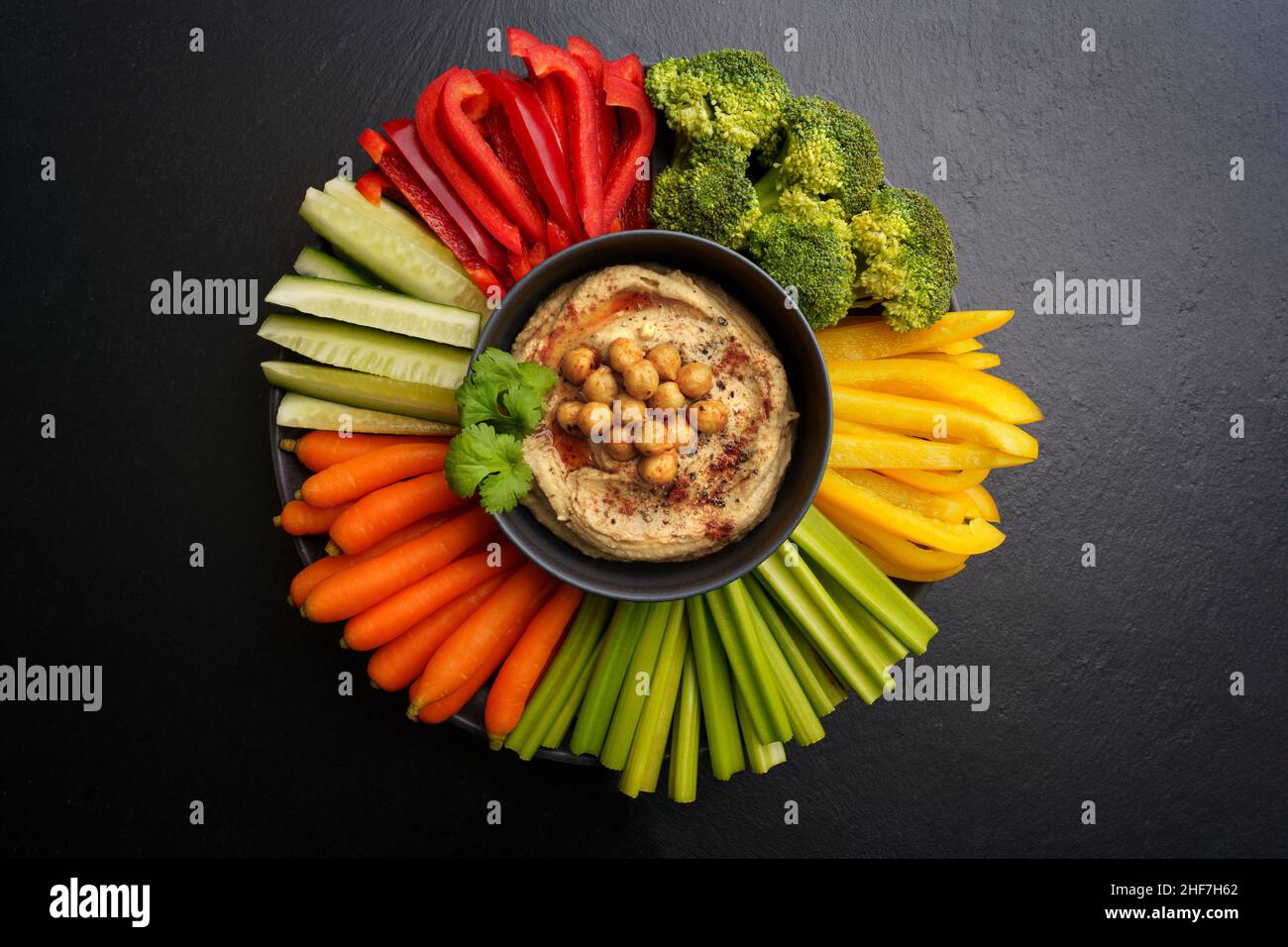 Draufsicht auf leckere Kichererbsen Hummus in schwarzem Teller mit frischem Gemüse auf schwarzem Hintergrund Stockfoto