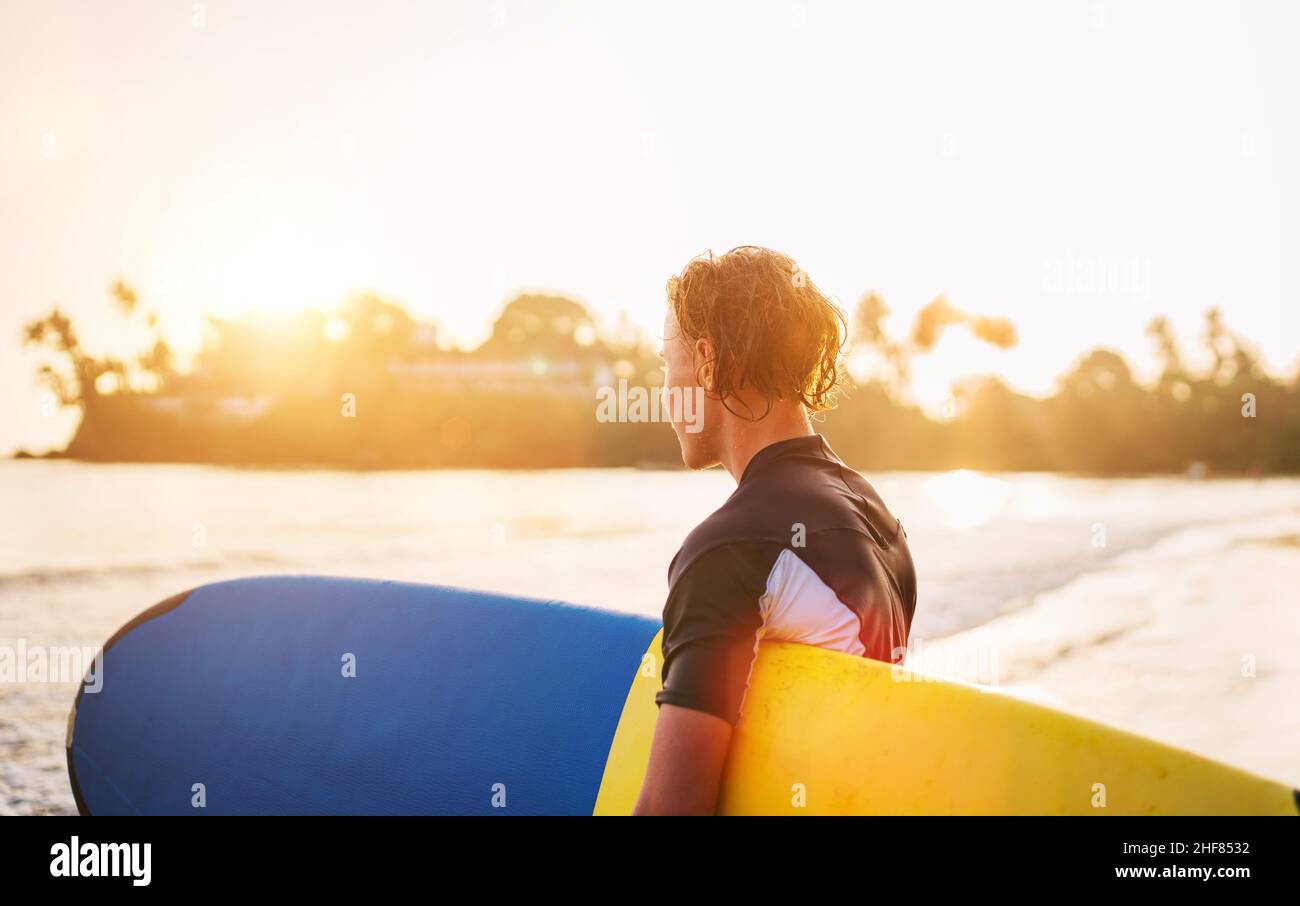 Junger Teenager Junge mit buntem Surfbrett geht zum Surfen ins Meer. Er genießt ein wunderschönes Sonnenuntergangslicht am Dewata Strand auf Sri Lanka. Aktiver Sport Stockfoto