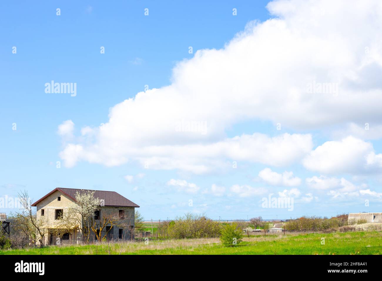 Ländliche Landschaft. Haus im Bau im Dorf und blauer Himmel mit Wolken an einem sonnigen Frühlingstag. Stockfoto