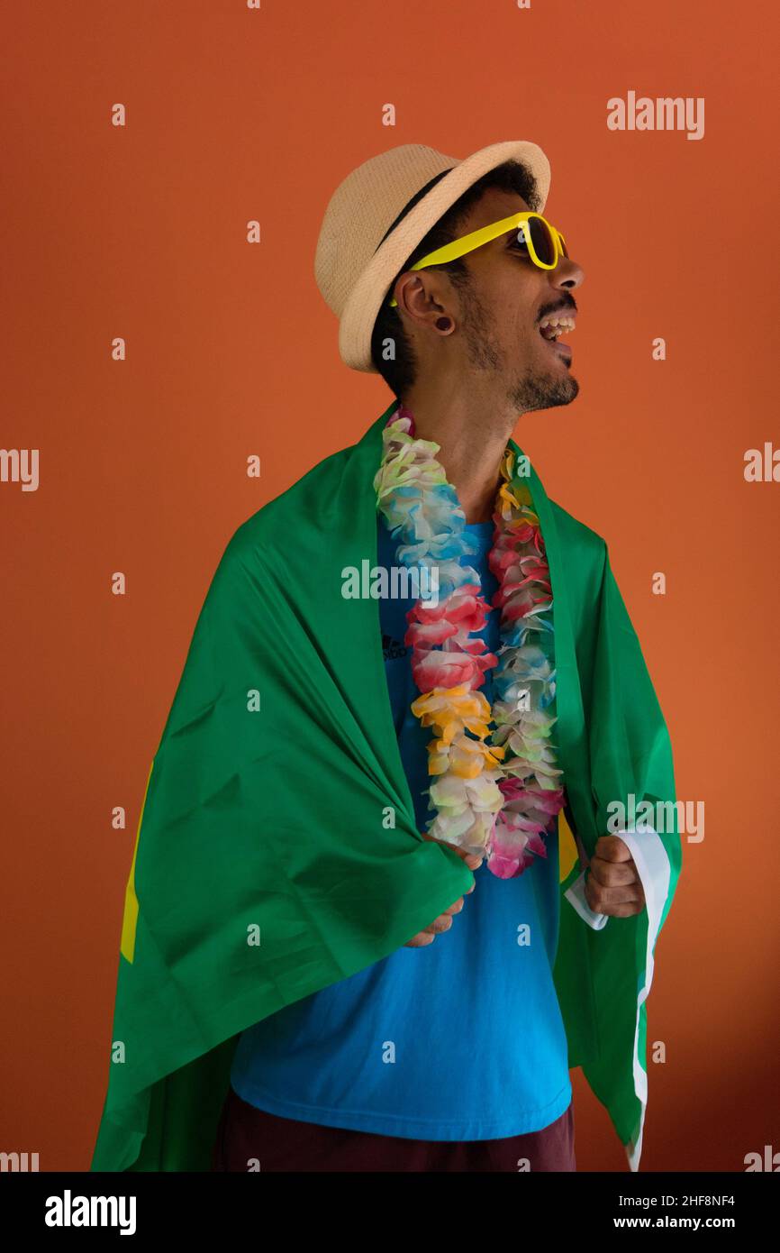 Schwarzer Mann im Kostüm für Karneval mit brasilien-Flagge isoliert auf orangefarbenem Hintergrund. Stockfoto