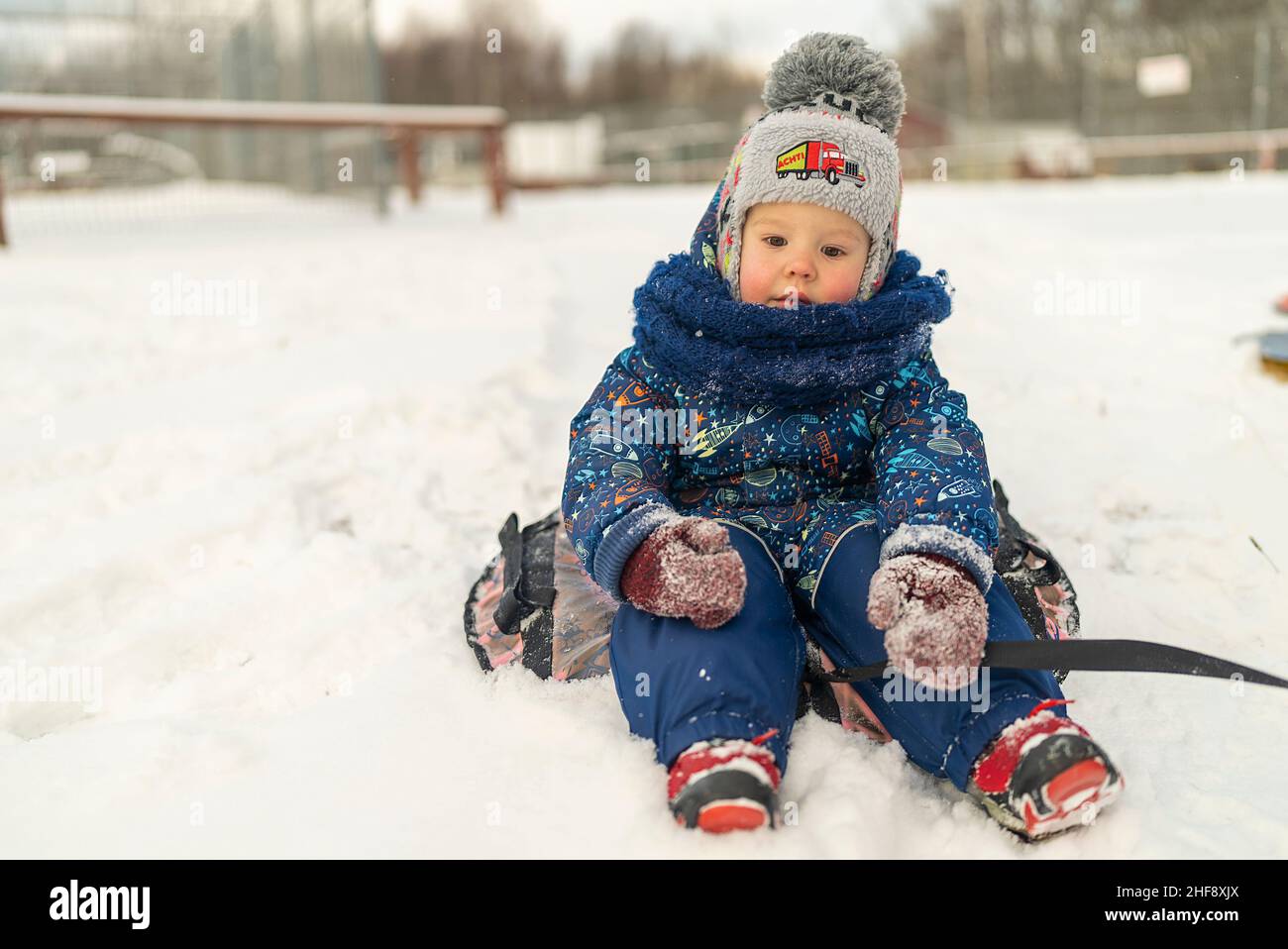 Der kleine Junge sitzt auf dem Schlauch in einer schneebedeckten Rutsche Winterspaß Stockfoto