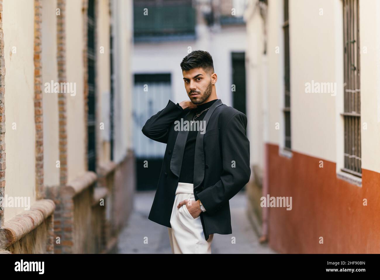 Attraktiver junger Mann posiert mit schwarzer Jacke und weißer Hose auf der Straße Stockfoto