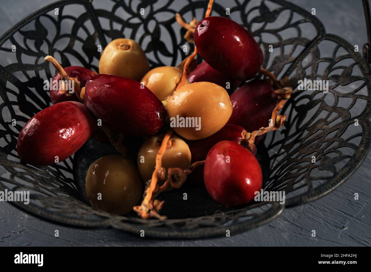 Rote und gelbe Rohdaten Obst oder Kurma Muda (Ruthob) auf Vintage Basket über rustikalem Hintergrund. Stockfoto