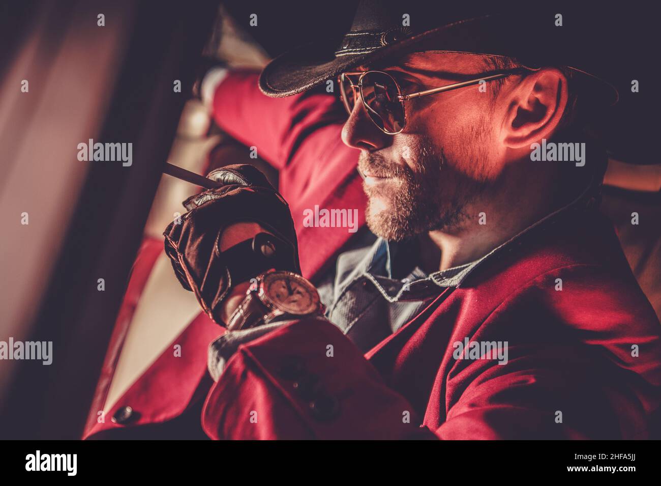 Der kaukasische amerikanische Cowboy trägt einen burgundischen Anzug, eine Sonnenbrille und einen Hut. Porträt Im Oldtimer. Stockfoto