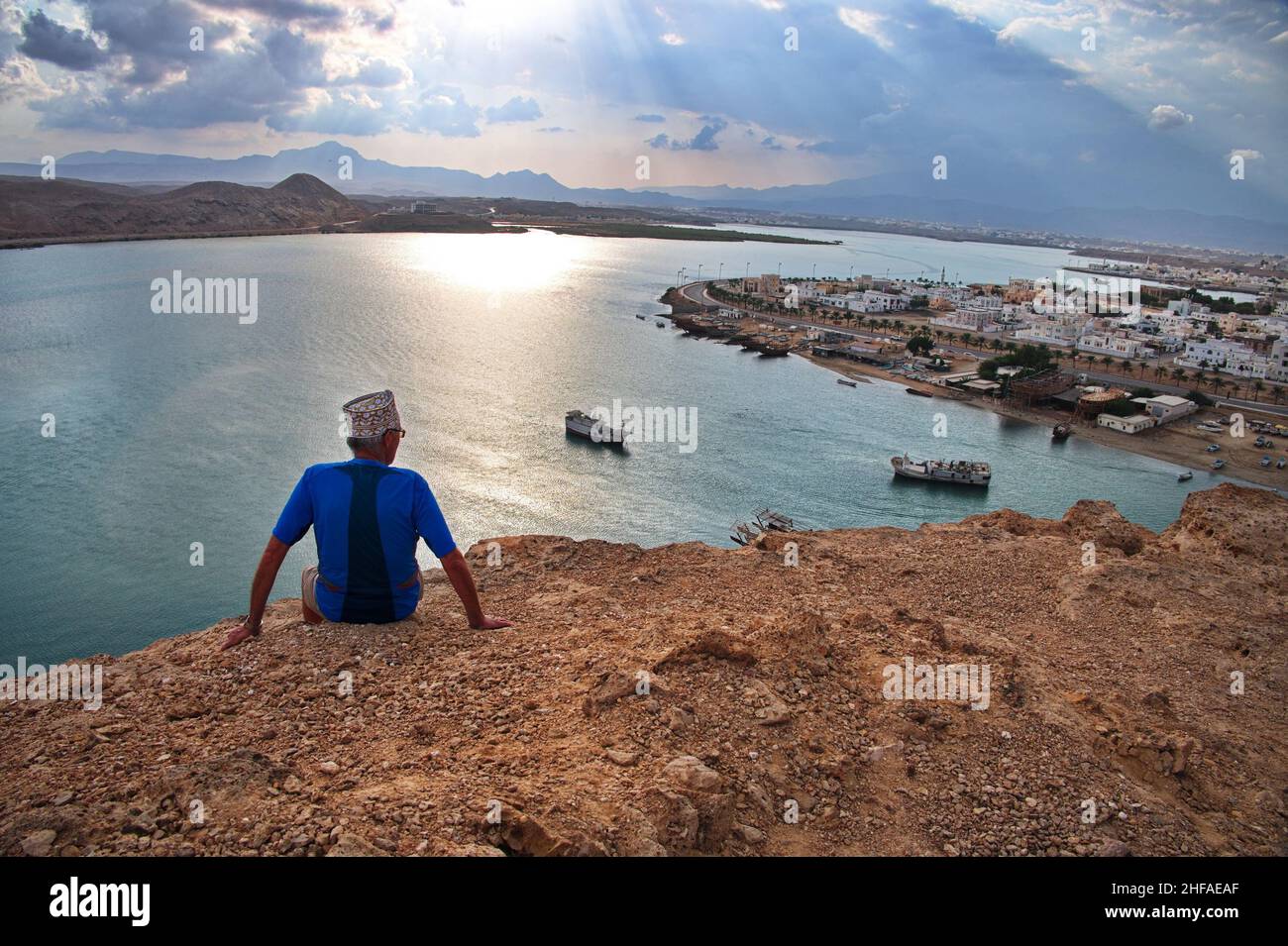 Seniortourist mit Oman Hut über der Bucht von Sur mit traditionellen Holzbooten im Hintergrund Stockfoto