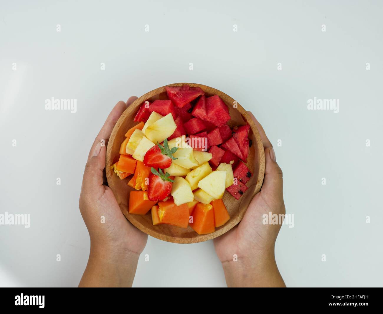 Hand hält gemischte Früchte auf einem Holzteller auf weißem Hintergrund. Gesundes Fruchtkonzept mit Kopierraum. Stockfoto