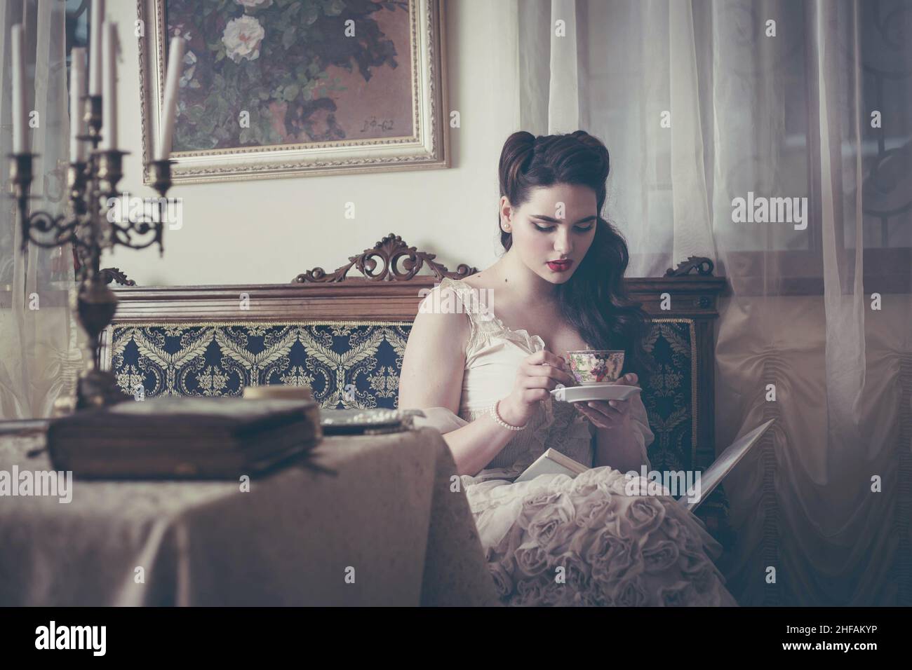 Die junge Frau trinkt Tee und liest in einem Vintage-Interieur ein Buch. Stockfoto