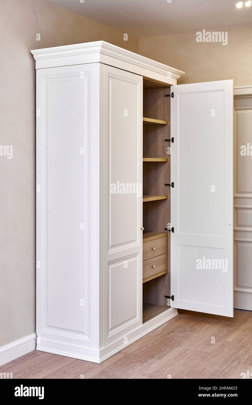 Weißer Vintage-Kleiderschrank mit Stuckverzierungen aus Holz, Regalen und  Schubladen und offener Fassadentür in hellem leerem Raum in einem  luxuriösen Apartment Stockfotografie - Alamy