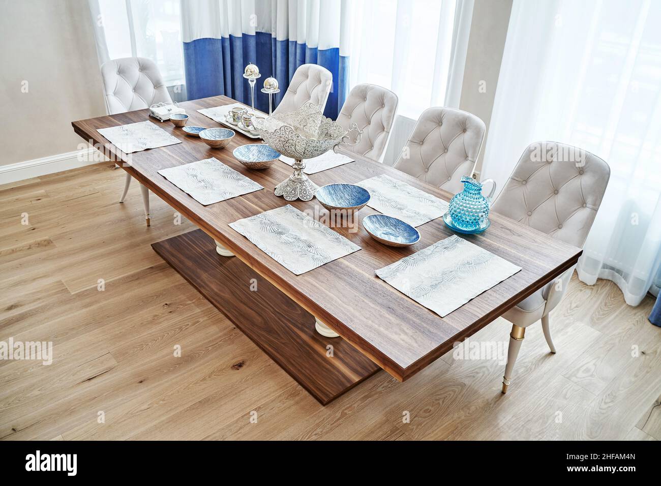 Luxuriöser Vintage-Esstisch aus massivem Nussbaum- und Furnierholz mit festlichem Ambiente und Sesseln in der Nähe des Fensters in einem geräumigen Zimmer Stockfoto