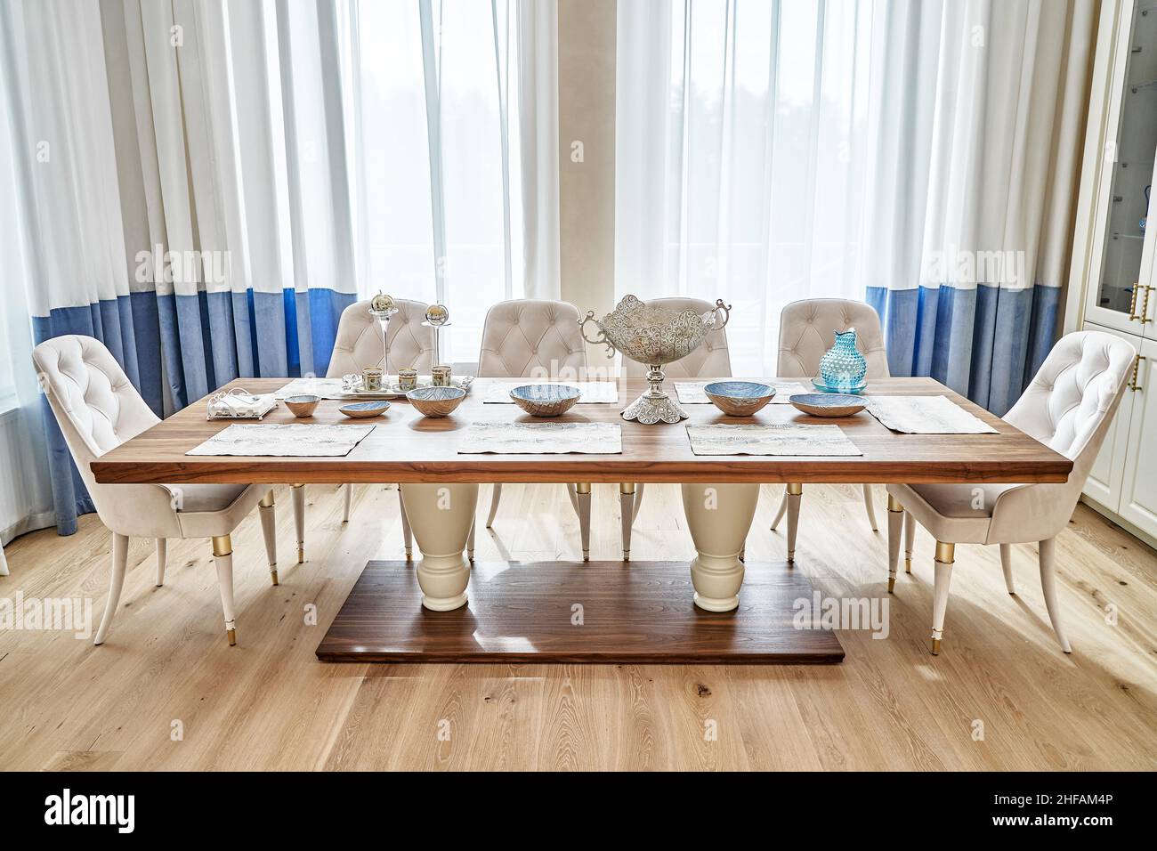 Luxuriöser Vintage-Esstisch aus massivem Nussbaum- und Furnierholz mit festlichem Ambiente und Sesseln in der Nähe des Fensters in einem geräumigen Zimmer Stockfoto
