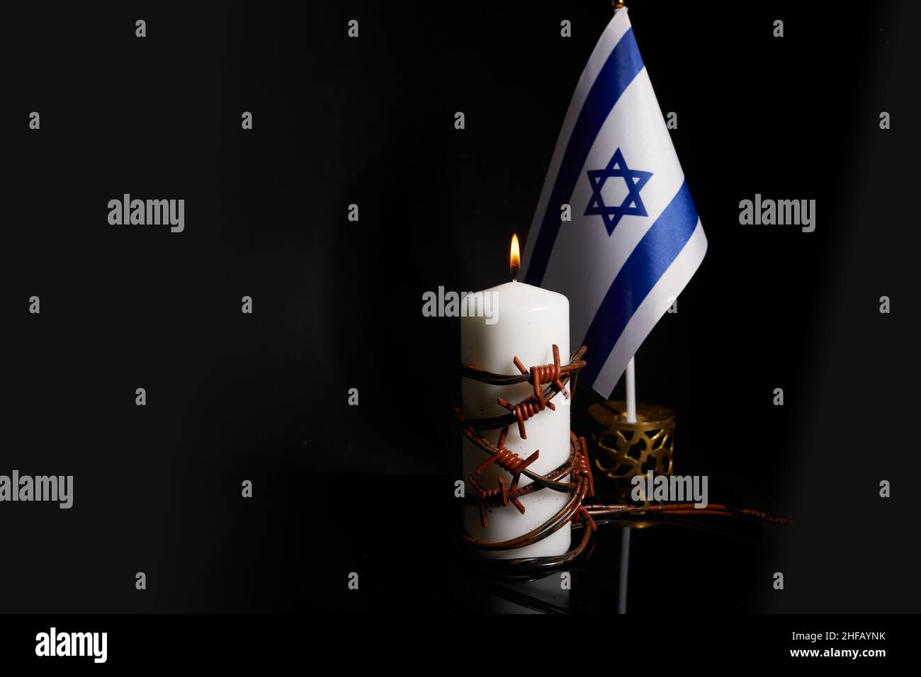 Stacheldraht auf brennender Kerze und israelische Flagge auf schwarzem Hintergrund mit Platz für Text. Holocaust-Gedächtnistag Stockfoto