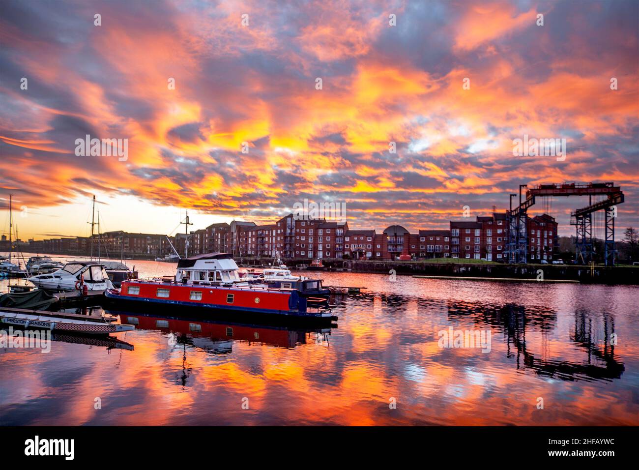 Sonnenaufgang am Preston Docks, Lancashire. Wetter in Großbritannien. 15 Jan, 2022., außergewöhnliche Cirrocumulus-Wolkenformationen, die sich an einem kalten Januarmorgen bei Sonnenaufgang in Preston-Docks bei kühltem Wind widerspiegeln. Cirrocumulus und Altocumulus rote Wolken enthalten überkühltes Wasser, das noch nicht zu Eiskristallen geworden ist. Das Wasser bleibt in der Atmosphäre schweben, bis sich schließlich Eiskristalle bilden und die umgebenden Wassertröpfchen verdunsten. Victoria Quay - Navigation Way Wohnungen in Docklands Reflexionen. Quelle: MediaWorldImages/AlamyLiveNews Stockfoto