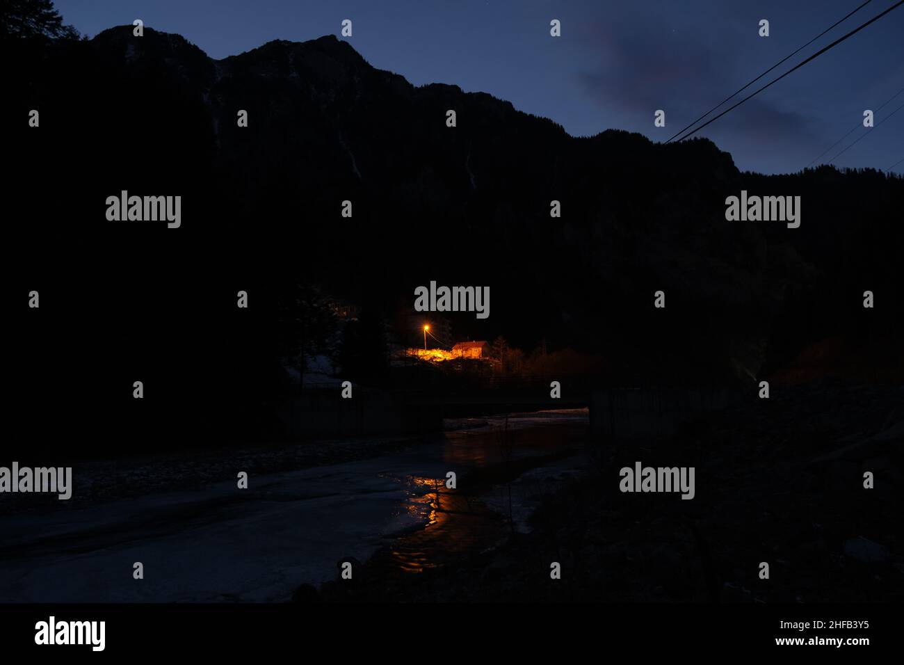 Nachtfoto, Straßenlaterne, gelbes Straßenlicht und einzelnes Dorfhaus, Beleuchtung und Reflexion auf dem Fluss in der Nacht- und Wintersaison. Stockfoto