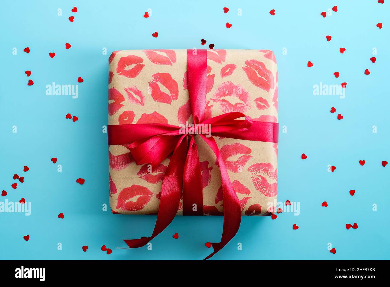 Geschenkbox mit rotem Band auf blauem Hintergrund mit Konfetti gebunden. Happy Valentines Day Konzept. Stockfoto