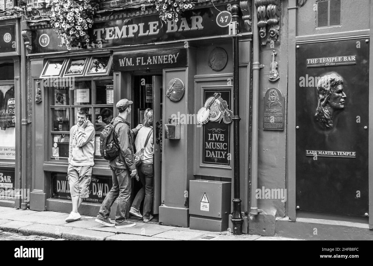 Zwei Jugendliche betreten die Temple Bar in Dublin, ein weiter männlicher Jugendlicher telefoniert in lässiger Haltung mit seinem Smartphone Stockfoto