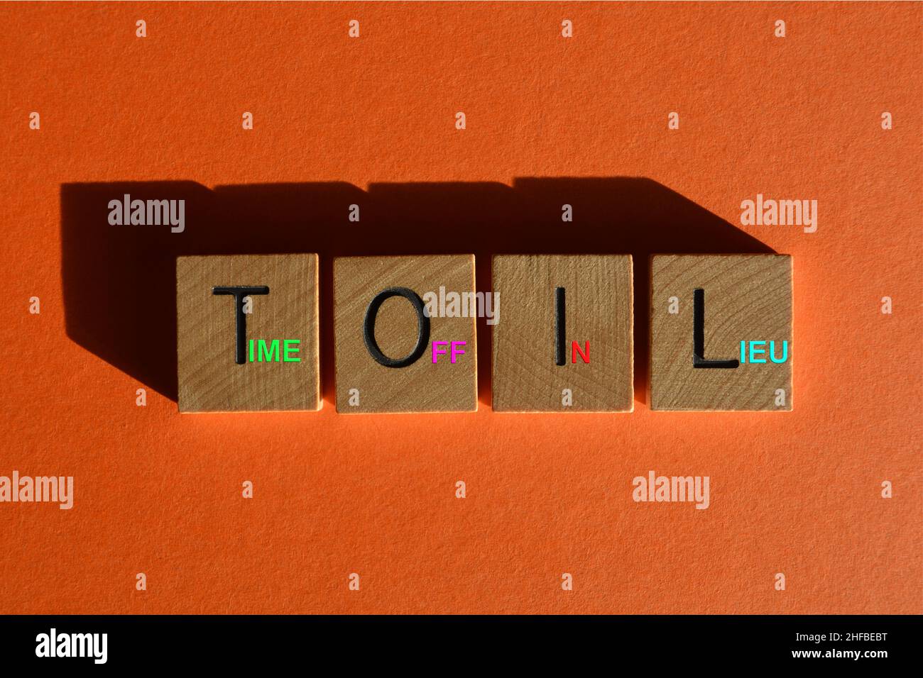 Toil, Akronym für Time Off in Lieu, Wörter auf hölzernen Buchstaben auf orangefarbenem Hintergrund Stockfoto