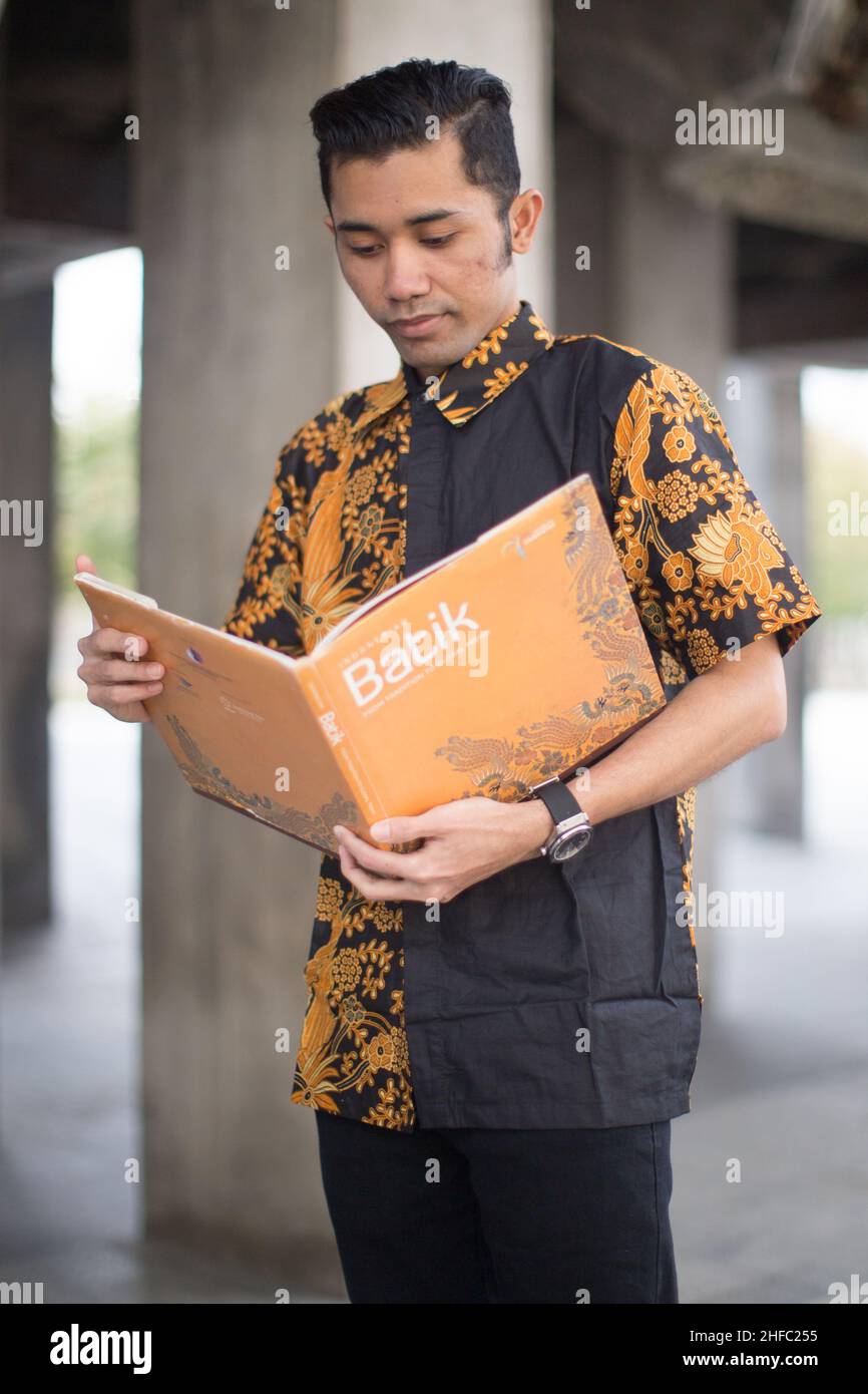 Ein junges männliches Model in indonesischer Batik liest im Long Museum, West Bund, Shanghai China, ein Buch mit dem Titel Batik Stockfoto