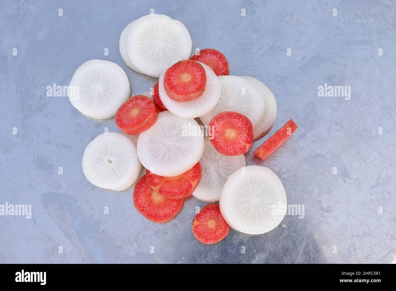 Nahaufnahme des Bündels in Scheiben geschnittene rote Karotte mit weißem Rettich über unscharf grauem Hintergrund. Stockfoto