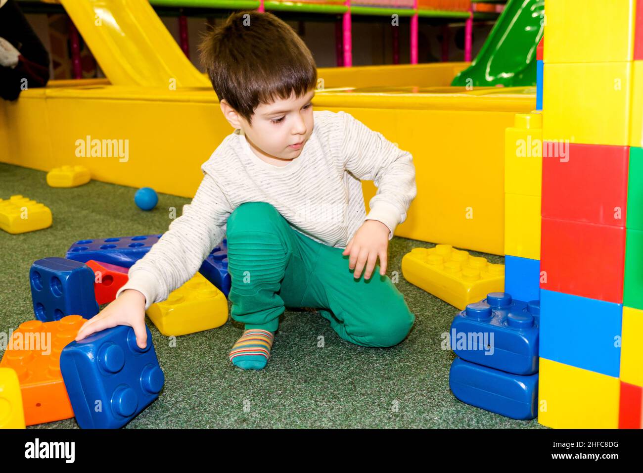 Ein Vorschuljunge spielt mit großen Baublöcken im Spielzimmer, einem Kinderanimationszentrum und einem Indoor-Spielplatz. Stockfoto
