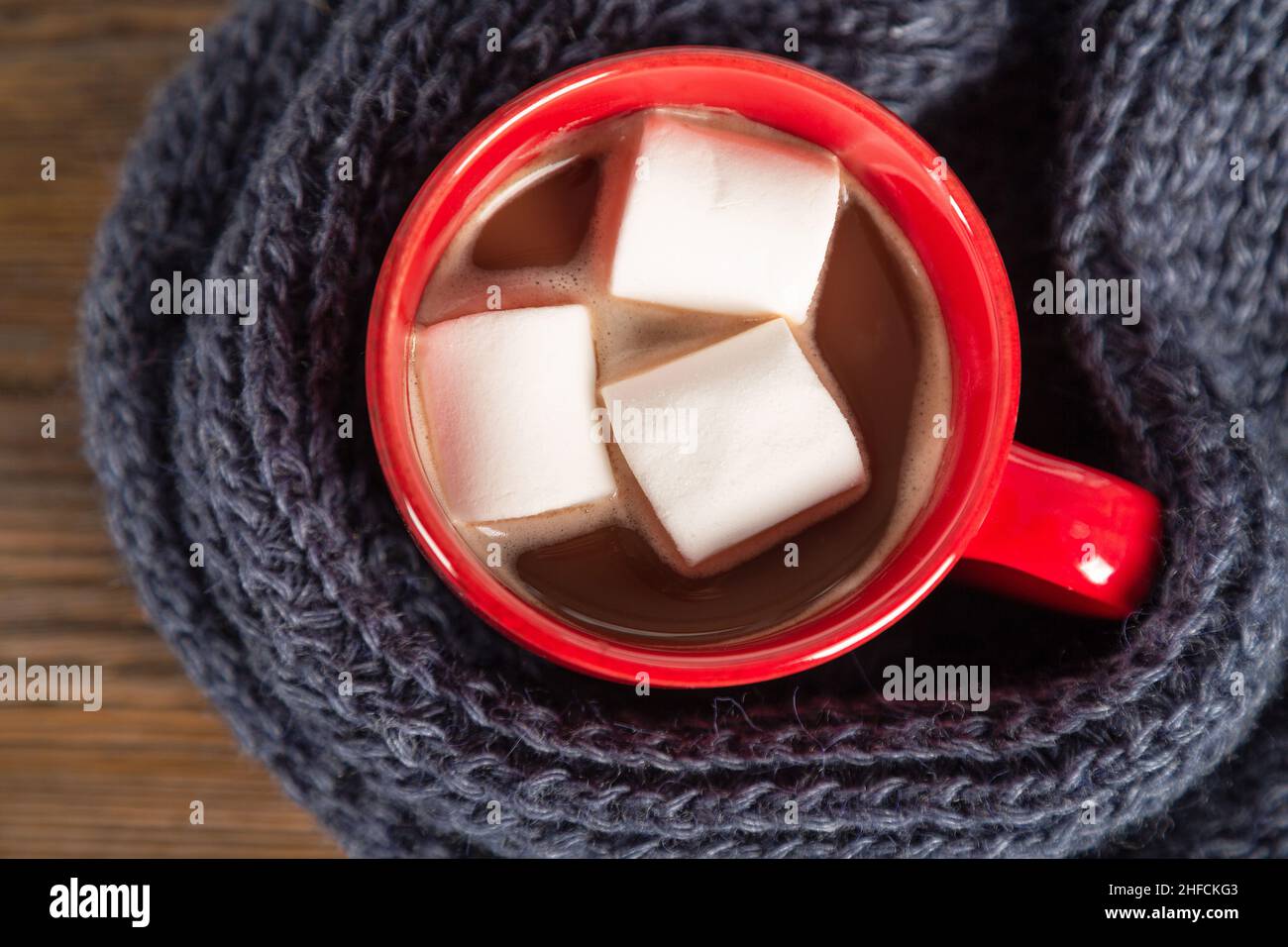 Weihnachten und Winter gemütlicher Hintergrund mit Strickschal und rotem Becher mit Kakao oder heißer Schokolade. Flach liegend, Draufsicht Stockfoto
