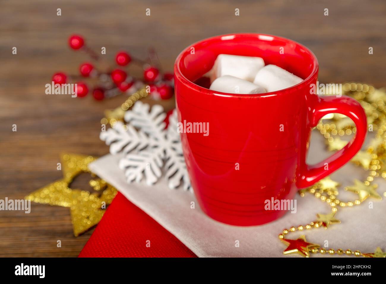 Heiße Schokolade oder Kakao in einem roten Becher und goldene Dekorationen auf braunem Holzhintergrund. Weihnachten und Neujahr traditionelle Küche. Stockfoto