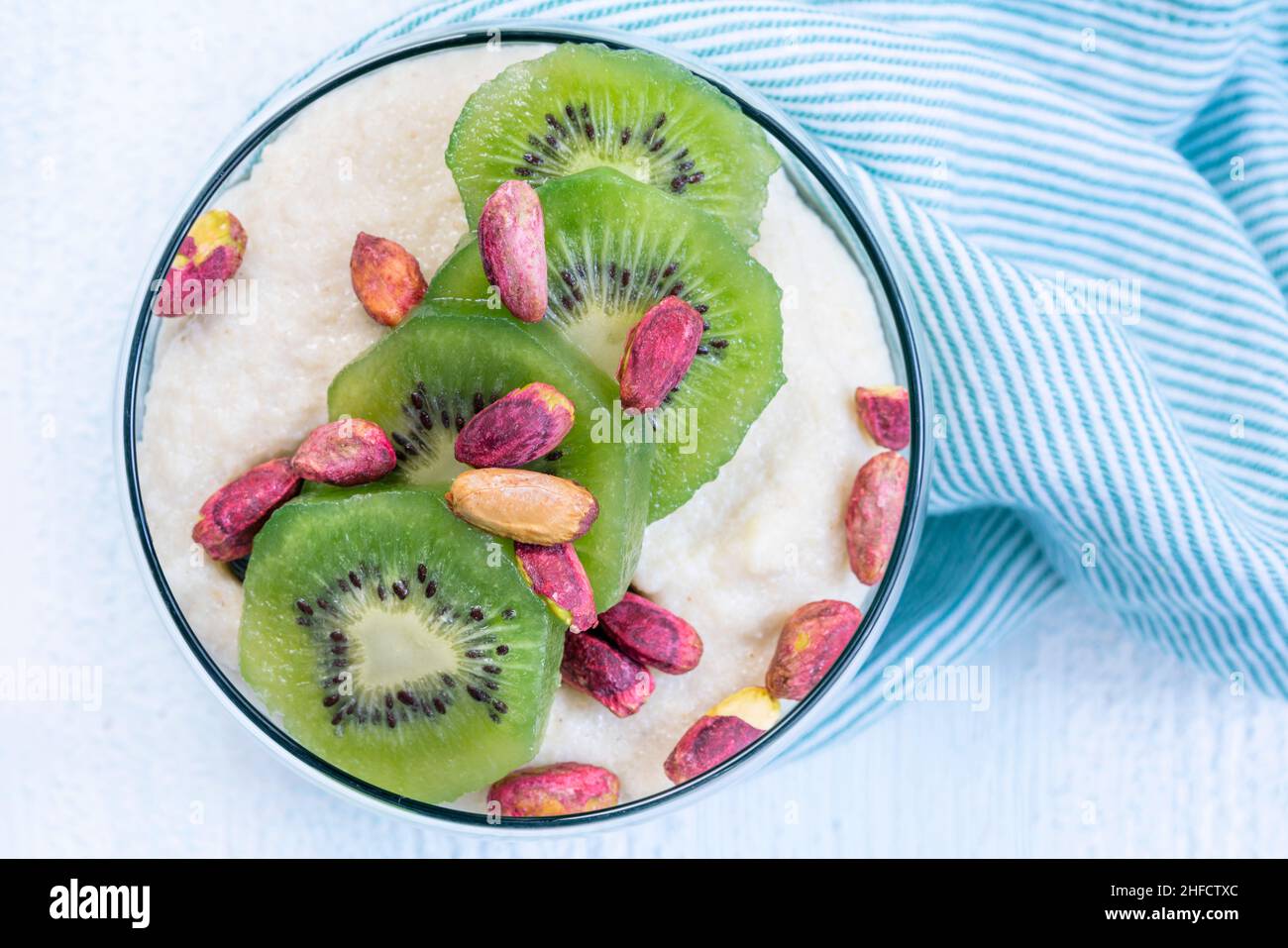 Pudding Dessert, hausgemachter Vanillepudding oder Joghurt mit Kiwi-Früchten und Pistazien auf dem Tisch. Draufsicht Schüssel Joghurt mit Früchten zum Frühstück Stockfoto