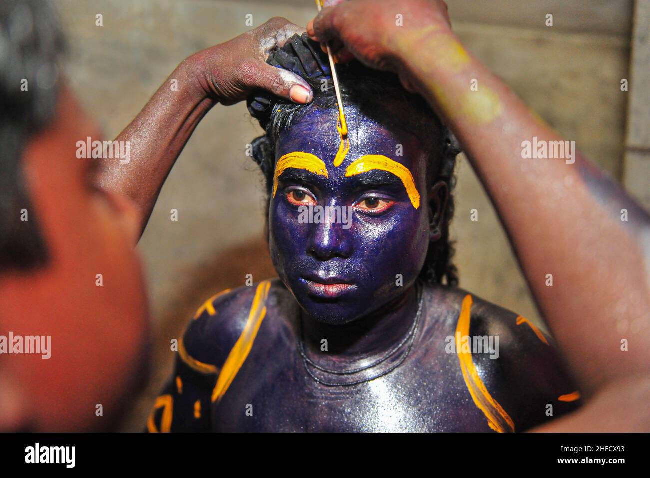 Ein eifriger Anhänger, der sich für das Charak Puja Festival während des Poush Shonkhanti of Bangladesh Kalenderjahres schminkt. Körpermalerei ist ein Teil des ri Stockfoto