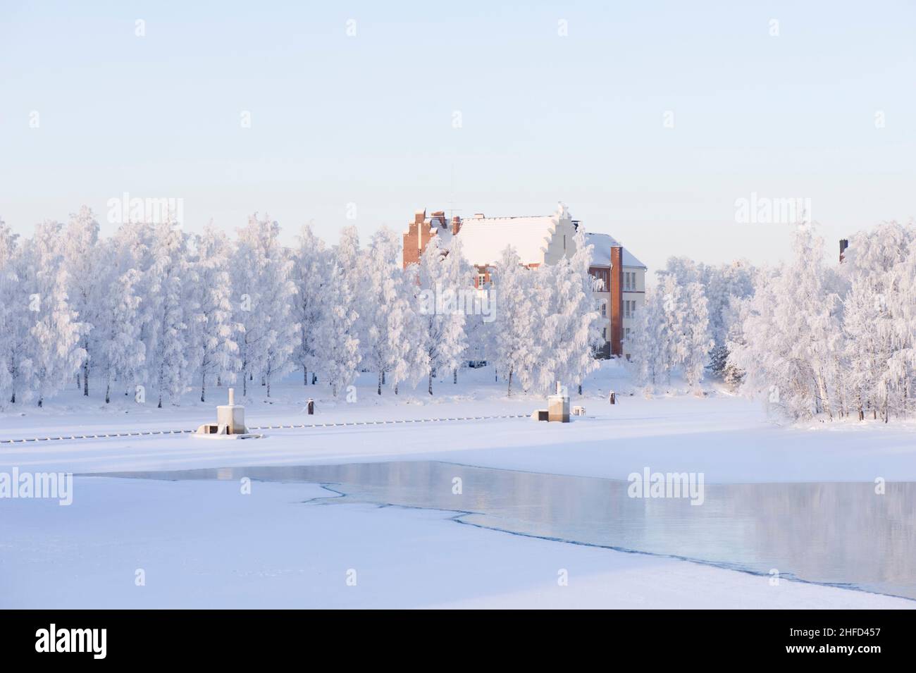 Winterlandschaft mit frostbedeckten Bäumen und altem Gebäude am Flussufer Stockfoto