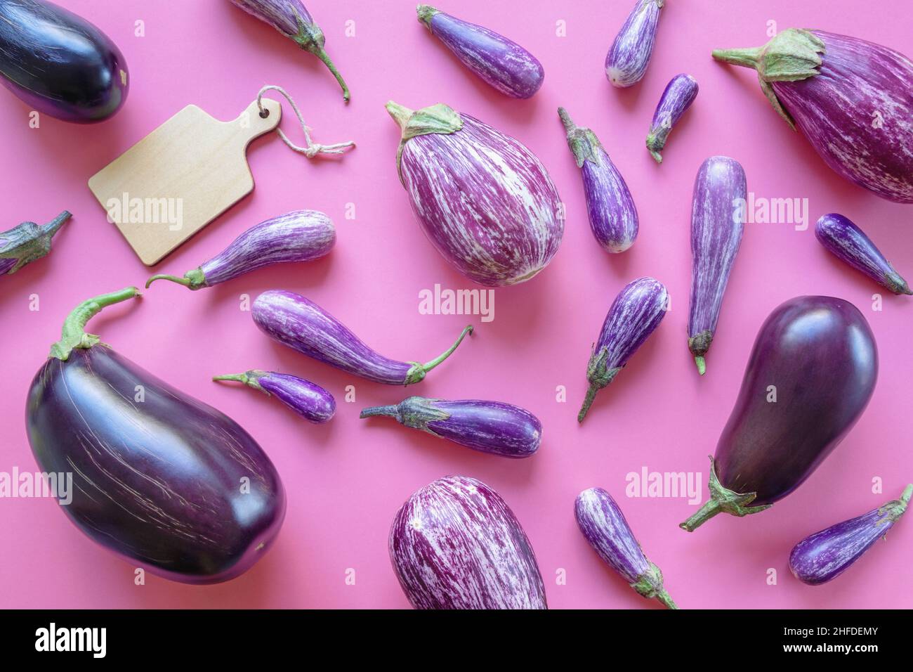 Verschiedene Sorten Auberginen und Schneidebrett auf rosa Hintergrund Stockfoto