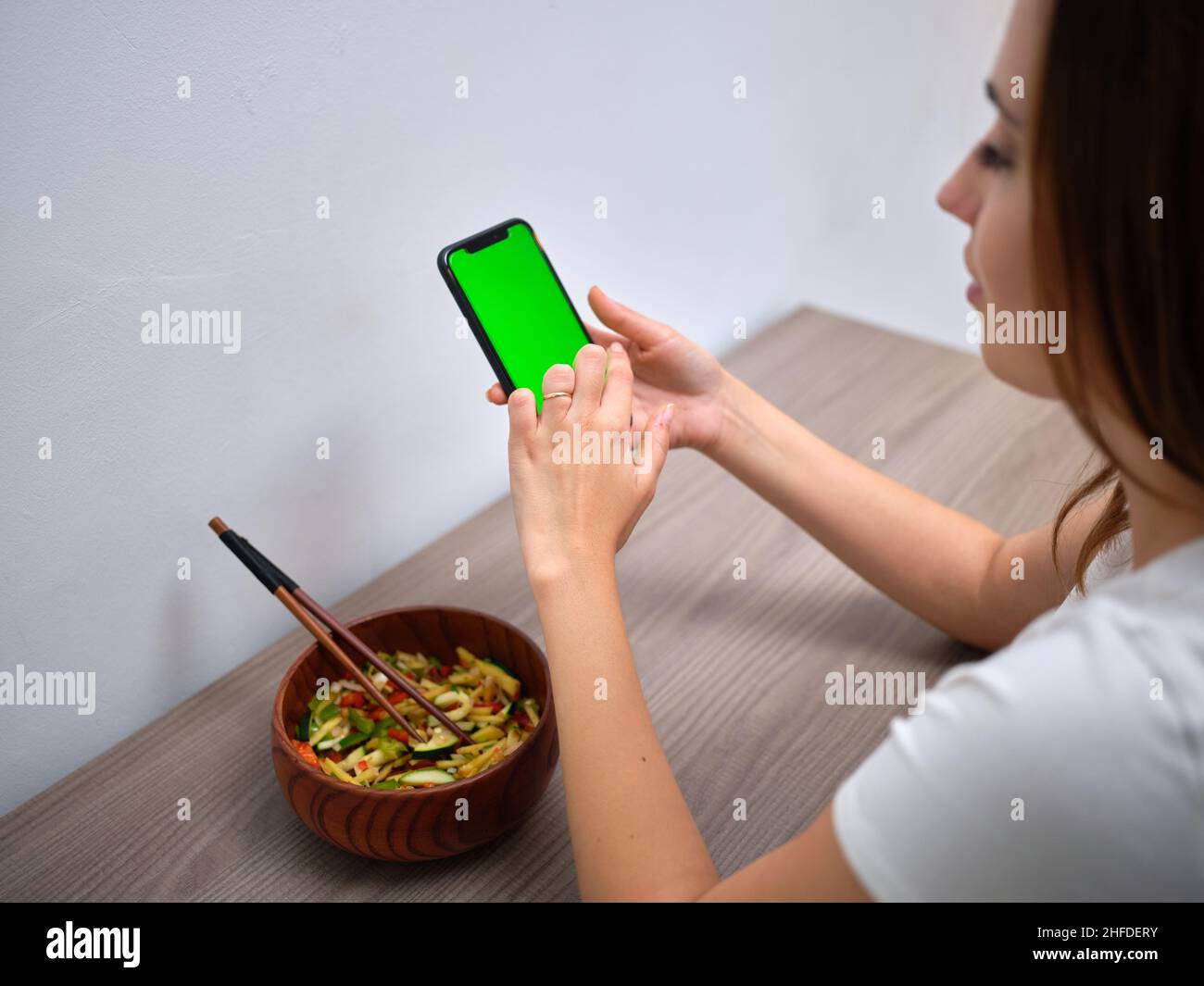 Frau, die am Tisch sitzt und auf den grünen Bildschirm ihres Mobiltelefons schaut Stockfoto