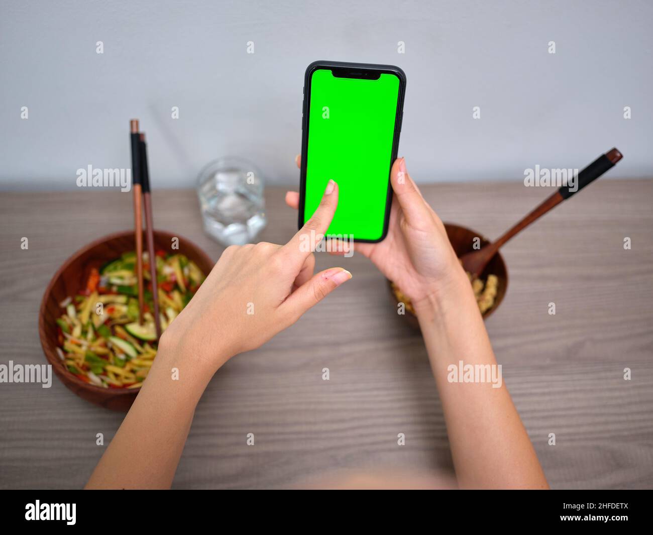 Weibliche Person, die orientalisches Essen isst, während sie auf den grünen Bildschirm ihres Telefons zeigt Stockfoto