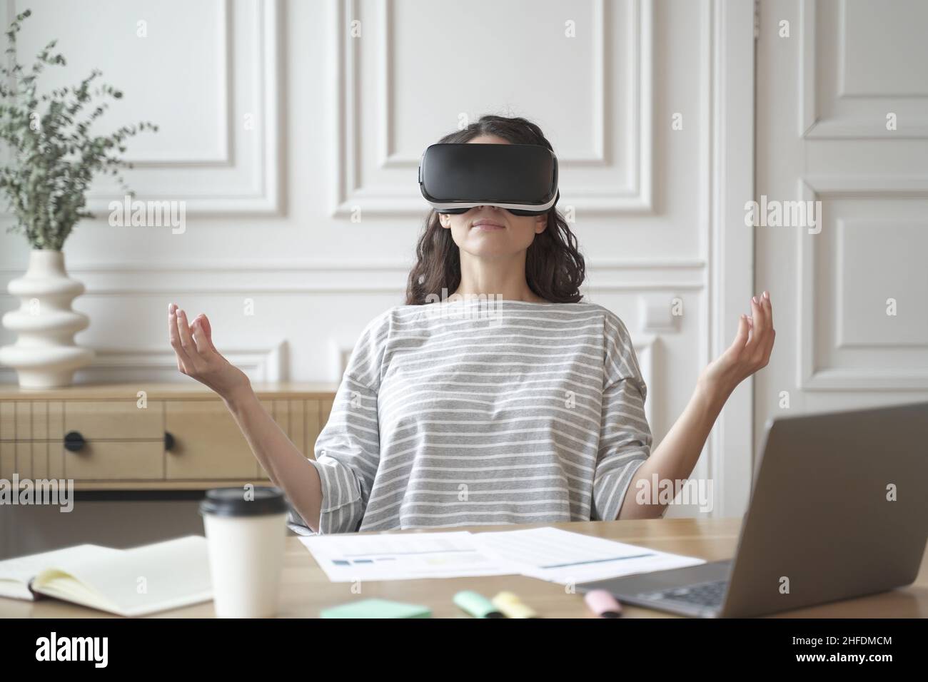 Friedliche Angestellte, die in einer Brille der virtuellen Realität meditiert und in Zen-Pose am Arbeitsplatz sitzt Stockfoto