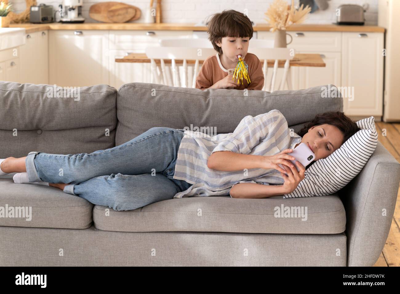 Ruhige junge Frau Mutter, Kindermädchen ignorieren laute Kind auf dem Sofa liegend mit Smartphone chatten in Apps Stockfoto