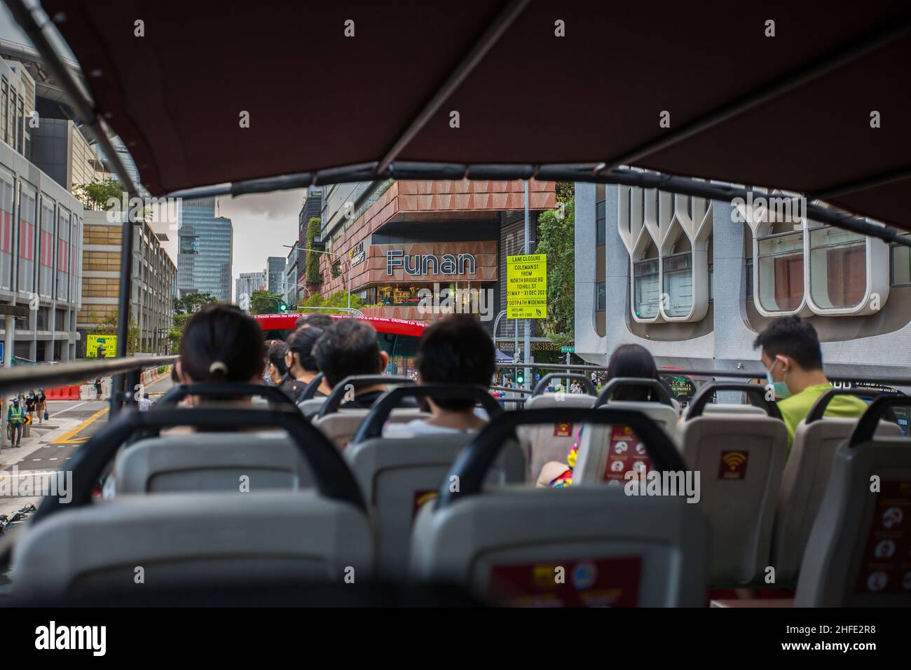 In einem Doppeldeckerbus mit offenem Oberdeck, der mit Touristen gefüllt ist und die Funan Mall überblickt, die entlang der North Bridge Road fährt. Singapur. Stockfoto