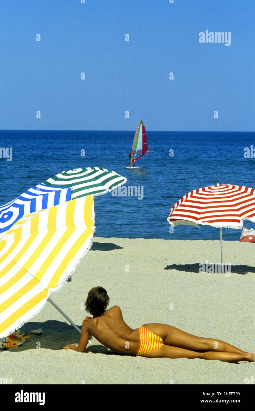 Blonde Haare junge Schönheit Rückansicht Legen Sie sich auf Sand gelb Badeanzug Schlankheit blauen Himmel Meerwasser Palmen Hintergrund Stockfoto