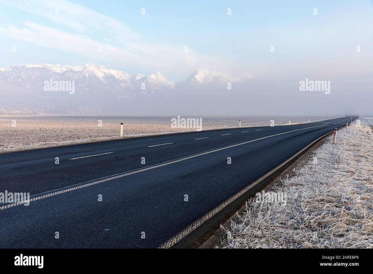 Leere Straße und schneebedeckte Gipfel der Kamnik-Savinja Alpen, die im morgendlichen Frost ihren Höhepunkt aus Nebel erreichen, Menges, Slowenien Stockfoto