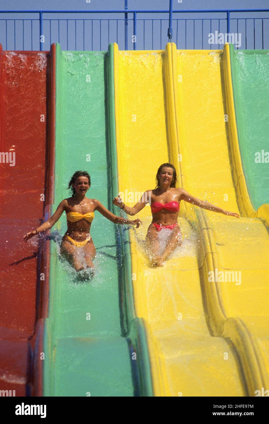 2 junge Frauen slidng auf farbigen Rodel frohe Feiertage lustigen Look Stockfoto
