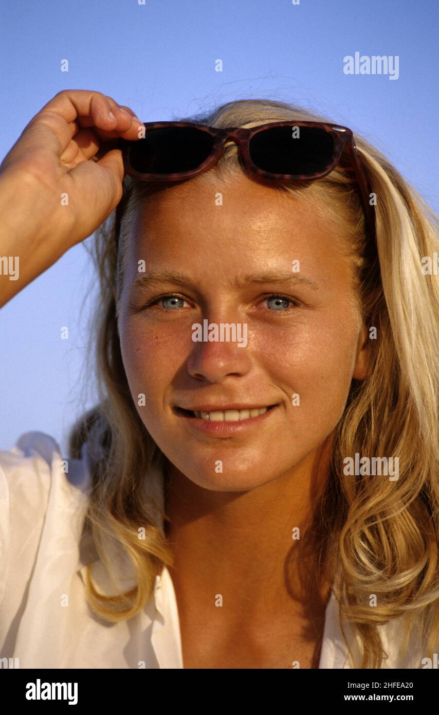 Blonde Haare ausdrucksstark lächelnd glücklich junge Frau Porträt aussehende Frontkamera mit Suglasses blauen Himmel Hintergrund Stockfoto