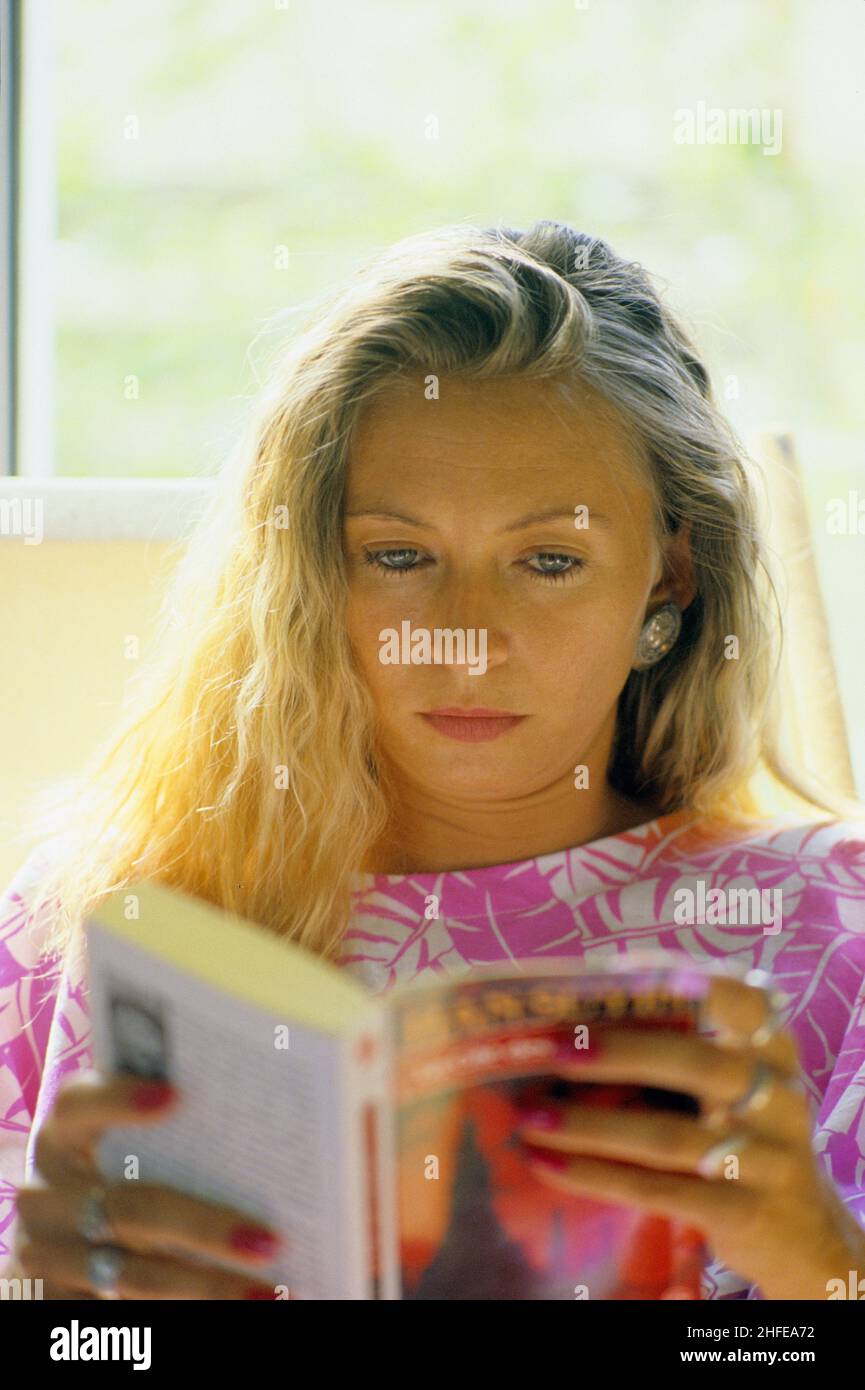 Blonde Haare junge Frau Porträt vorne Kamera lesen Buch Unterlicht Fenster Stockfoto