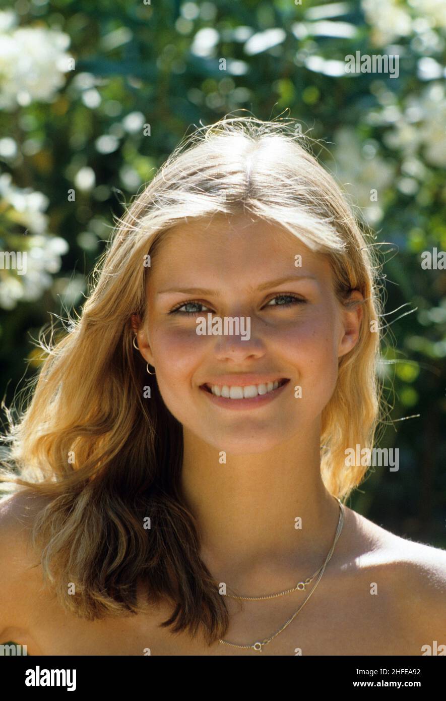 Blonde Haare ausdrucksstark lächelnd glücklich junge Frau Porträt suchen Frontkamera unterhellgrün natürlichen Laub Hintergrund Stockfoto